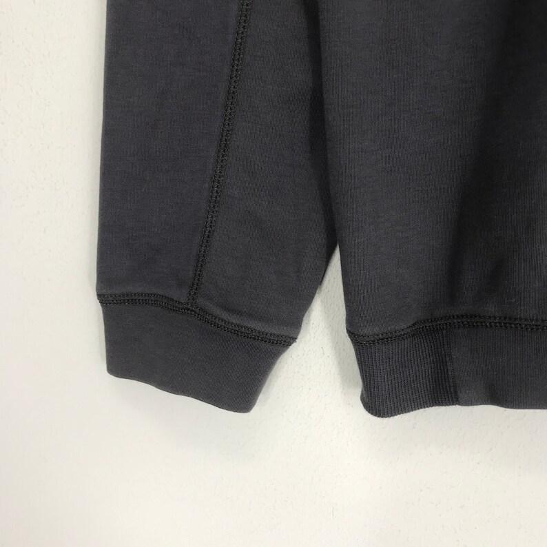 Peut inclure: Un sweat-shirt gris fonc&eacute; &agrave; manches longues et poignets c&ocirc;tel&eacute;s. Le sweat-shirt a un design uni sans graphismes ni texte visibles.
