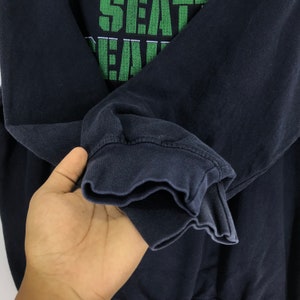 Puede incluir: Sudadera negra de manga larga con texto bordado en verde que dice "Seattle Seahawks".
