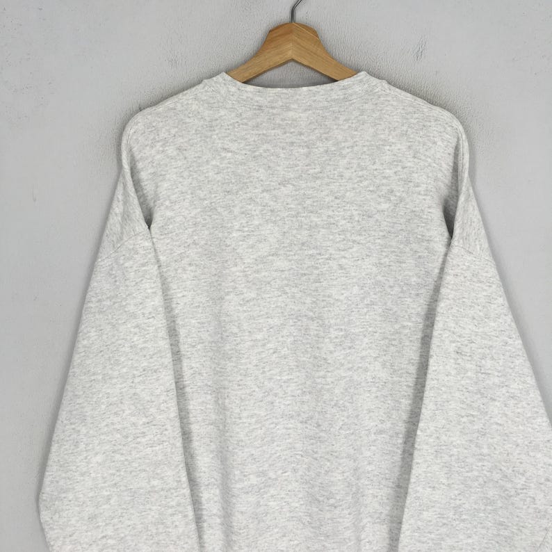 May include: A heather gray sweatshirt hangs on a wooden hanger. The sweatshirt has a crew neck and long sleeves. The fabric appears to be a soft, comfortable material. The garment is displayed against a plain gray background.