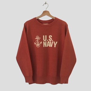Könnte beinhalten: Ein roter Pullover mit einem weißen Anker und dem Schriftzug "U.S. NAVY" auf der Vorderseite.