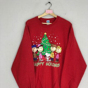 May include: Red sweatshirt with a Christmas tree and the Peanuts characters, including Snoopy, Charlie Brown, Lucy, Linus, and Sally. The text "Happy Holidays" is printed below the characters.