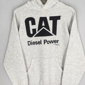 Puede incluir: Una sudadera con capucha de manga larga en color gris jaspeado claro que presenta un gran logotipo CAT negro impreso en el pecho. Debajo del logotipo, el texto dice Diesel Power en letras negras, con un peque&ntilde;o texto de copyright bajo la palabra Power.