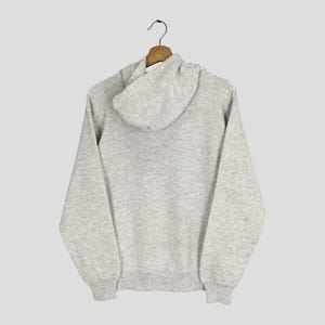 Puede incluir: Una sudadera con capucha de manga larga en color gris jaspeado claro, que cuenta con una capucha con cord&oacute;n, pu&ntilde;os acanalados en las mu&ntilde;ecas y un dobladillo acanalado en la cintura. La prenda se muestra desde atr&aacute;s, con la capucha sobre la espalda.