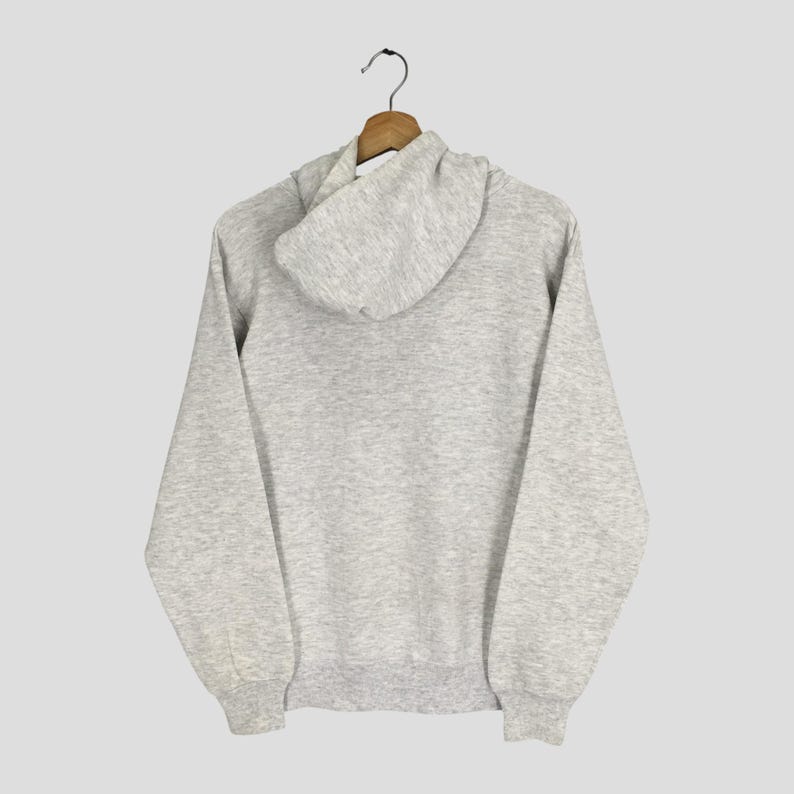 Puede incluir: Una sudadera con capucha de manga larga en color gris jaspeado claro, que cuenta con una capucha con cord&oacute;n, pu&ntilde;os acanalados en las mu&ntilde;ecas y un dobladillo acanalado en la cintura. La prenda se muestra desde atr&aacute;s, con la capucha sobre la espalda.