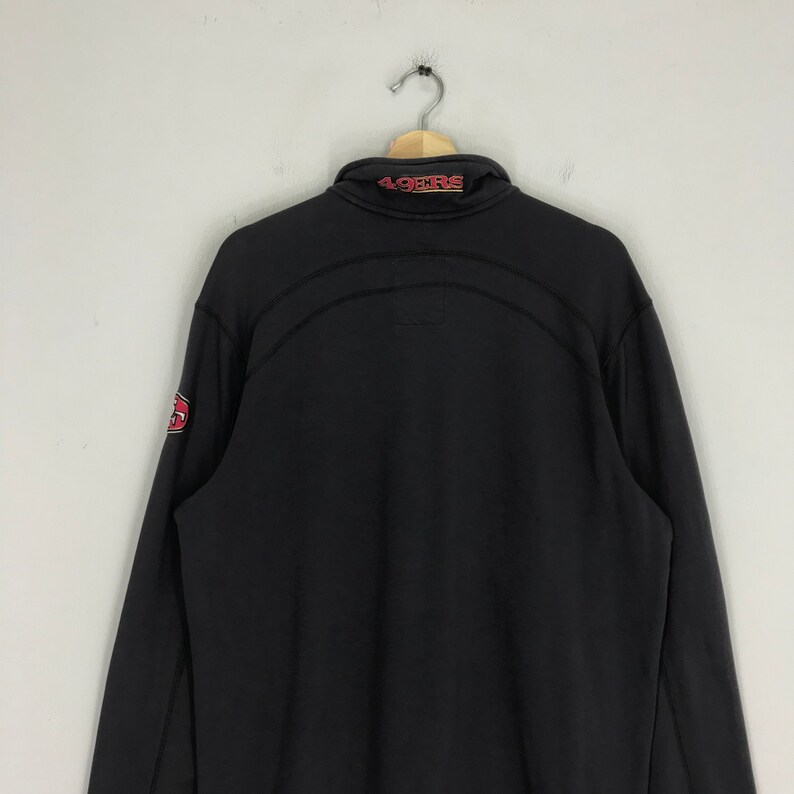 Peut inclure: Sweat-shirt &agrave; fermeture &eacute;clair noir &agrave; manches longues avec le mot "49ers" en rouge sur le col et un logo rouge et blanc sur la manche gauche.