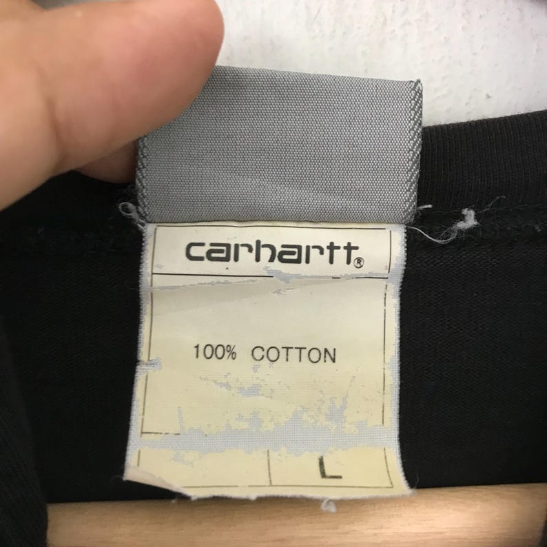 May include: A black Carhartt t-shirt with a white tag that says "Carhartt" and "100% Cotton" and has a size "L" label.