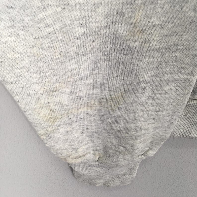 May include: Close-up of a light gray sweatshirt sleeve. The fabric has a textured appearance with some discoloration and stains. The cuff is ribbed and the overall garment appears to be well-worn.