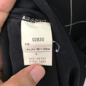 May include: A black clothing tag with white text. The tag says "02830", "Size", "Chest 96~104cm", "L", "ACE-05757", and "E752-1905".