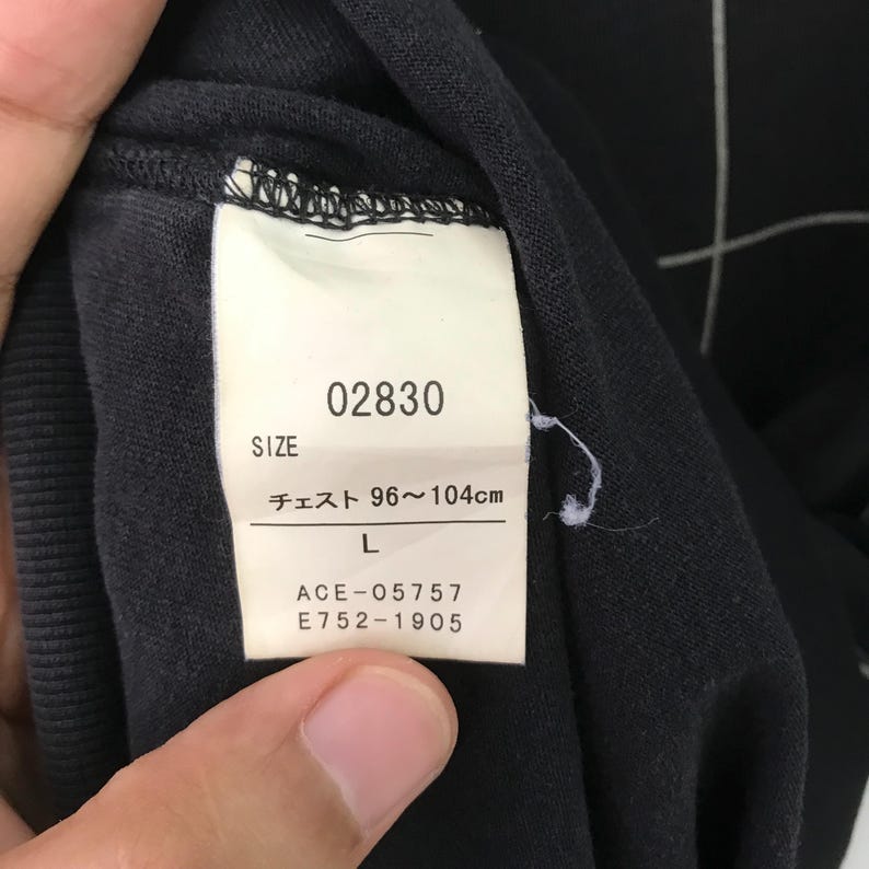 May include: A black clothing tag with white text. The tag says "02830", "Size", "Chest 96~104cm", "L", "ACE-05757", and "E752-1905".