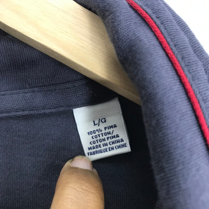 Peut inclure: Une &eacute;tiquette de polo en coton bleu avec des coutures rouges. L'&eacute;tiquette indique "L/G 100% PIMA COTTON/COTON PIMA MADE IN CHINA FABRIQUE EN CHINE".