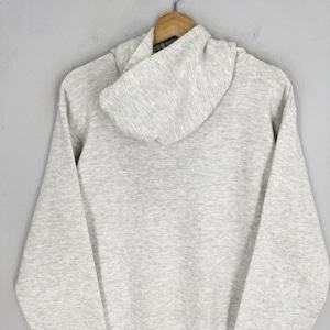 Puede incluir: Una sudadera con capucha de manga larga en color gris claro jaspeado, con capucha sin cordones, mangas largas con pu&ntilde;os acanalados y dobladillo acanalado. La prenda est&aacute; confeccionada en un tejido suave y moteado, colgada en una percha de madera.