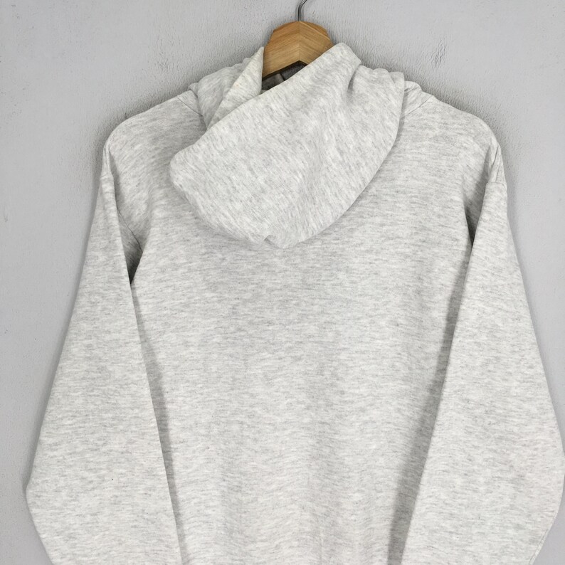 Puede incluir: Una sudadera con capucha de manga larga en color gris claro jaspeado, con capucha sin cordones, mangas largas con pu&ntilde;os acanalados y dobladillo acanalado. La prenda est&aacute; confeccionada en un tejido suave y moteado, colgada en una percha de madera.
