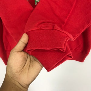 May include: Red sweatshirt with a ribbed cuff. The cuff is folded over twice.