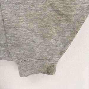 K&ouml;nnte beinhalten: Nahaufnahme eines grauen Sweatshirt-&Auml;rmels. Der Stoff hat eine melierte Textur mit einigen Verf&auml;rbungen. Das B&uuml;ndchen ist gerippt und weist Abnutzungserscheinungen auf. Der Hintergrund ist eine schlichte wei&szlig;e Oberfl&auml;che.