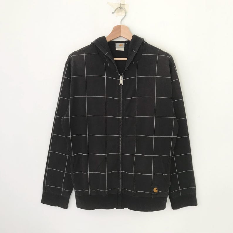 May include: Black hooded sweatshirt with a white grid pattern and a zipper closure. The sweatshirt has a small Carhartt logo patch on the bottom right side.