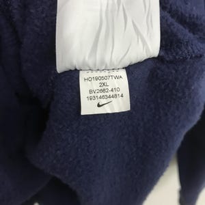 May include: A navy blue sweatshirt with a white tag that says "HO190507TWA 2XL BV2662-410 193146344814" and a Nike swoosh logo.