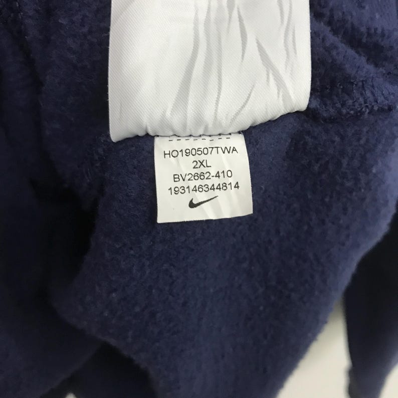 May include: A navy blue sweatshirt with a white tag that says "HO190507TWA 2XL BV2662-410 193146344814" and a Nike swoosh logo.