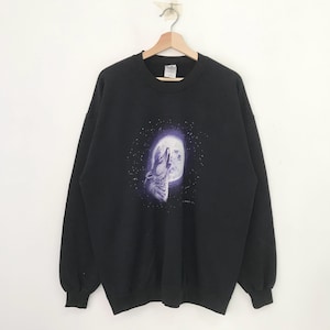 May include: Black sweatshirt featuring a graphic of a howling wolf in front of a full moon. The wolf and moon are in shades of purple and white, set against a starry night sky. The sweatshirt has a crew neck and long sleeves.