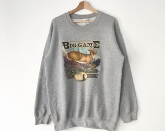 May include: Gray sweatshirt with a vintage-style print of a deer jumping over a log. The print says "American Naturals Big Game" with a small image of a hunter in the bottom left corner.