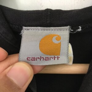 May include: A black Carhartt hoodie with a white tag that says "Carhartt" in red lettering and a yellow Carhartt logo.