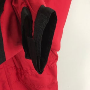 May include: Close-up of a red jacket with black elastic cuffs. The cuffs have a velcro closure.