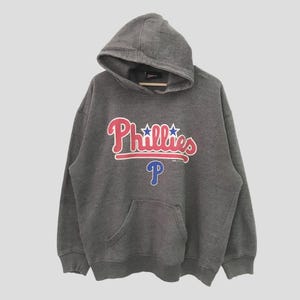 Könnte beinhalten: Ein grauer Kapuzenpullover mit dem Schriftzug "Phillies" in rot und blau und einem blauen "P"-Logo.