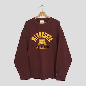 May include: Maroon crewneck sweatshirt with the word "MINNESOTA" arched across the chest in yellow lettering, with a yellow "M" logo and the words "GOLDEN GOPHERS" below. The sweatshirt is hanging on a wooden hanger.