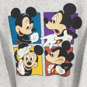 May include: A light gray sweatshirt featuring a colorful graphic of Mickey Mouse in four different poses. Each Mickey Mouse is set against a different colored square: blue, purple, yellow, and red. The graphic is centered on the front of the sweatshirt.