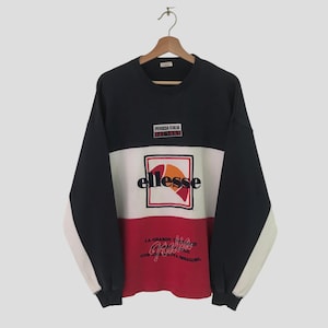 May include: A black, white, and red sweatshirt with the Ellesse logo in a white square on the front. The sweatshirt also has the text "PERUGIA ITALIA" and "LA GRANDE TRACCE" on the front.