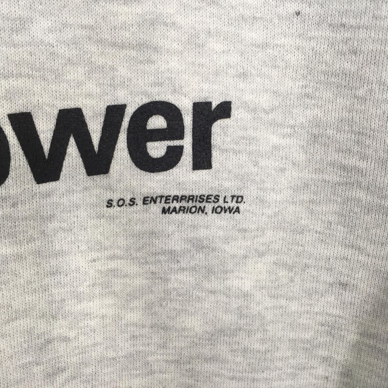 Puede incluir: Una tela jaspeada de color gris claro que presenta el texto impreso en negro "wer" y el texto m&aacute;s peque&ntilde;o en negro "S.O.S. ENTERPRISES LTD. MARION, IOWA" colocado justo debajo. El material tiene una textura de punto visible en toda la superficie.