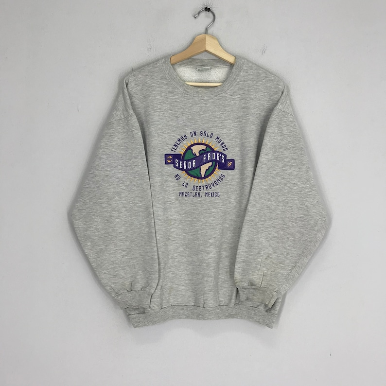 May include: Gray sweatshirt with a graphic print of a globe with the text "TENEMOS UN SOLO MUNDO SENOR FROGS NO LO DESTRUYAMOS MAZATLAN, MEXICO"