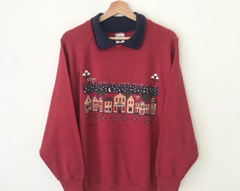 May include: Red sweatshirt with a navy blue collar and a graphic print of a small town at night with the text "Main St."
