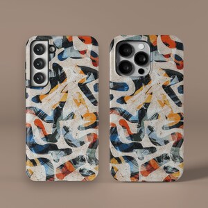 Può includere: Due custodie per telefono con un design astratto colorato che presenta pennellate nere, bianche, arancioni, gialle e blu. Le custodie sono realizzate per uno smartphone con un triplo obiettivo della fotocamera.