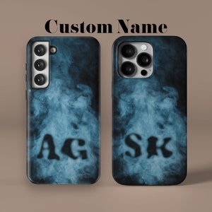 May include: Two phone cases with a blue smoke design and black letters. The left case has the letters "AG" and the right case has the letters "SK".