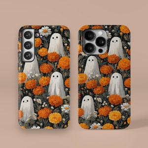 May include: Two phone cases with a repeating pattern of white cartoon ghosts, orange marigold flowers, and white daisies on a black background. The cases have a glossy finish and are designed for different phone models.