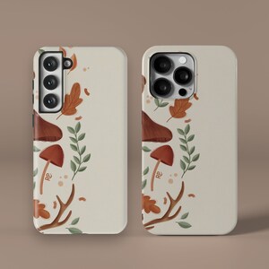 May include: Two phone cases with a cream background and an autumn-themed design. The design features mushrooms, leaves, and antlers in shades of brown, orange, and green.