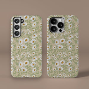 Può includere: Due custodie per telefono con un motivo di margherite bianche e foglie verdi su uno sfondo beige. Le custodie sono progettate per un telefono con un triplo obiettivo della fotocamera.