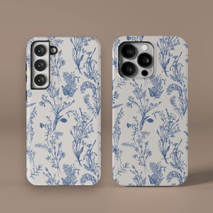 May include: Two phone cases with a white background and a blue floral pattern. The cases are for different phone models, one with a single camera and one with a triple camera.