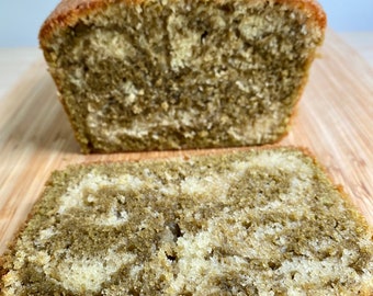 May include: A loaf of green tea pound cake sliced on a wooden cutting board. The cake has a marbled appearance with swirls of green tea and vanilla batter.
