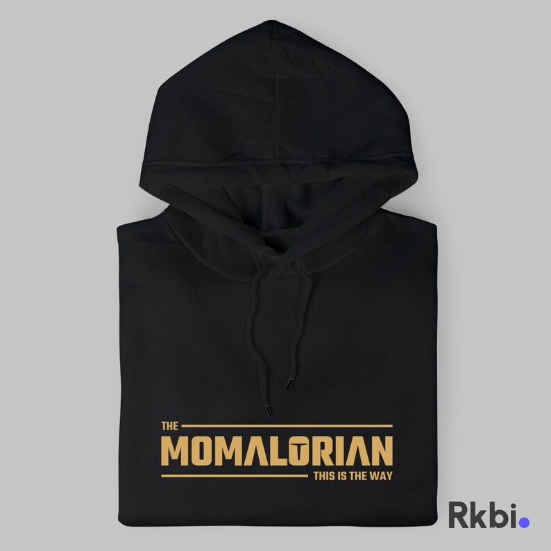 Pu&ograve; includere: Felpa con cappuccio nera con una grafica dorata che recita "THE MOMALORIAN THIS IS THE WAY".