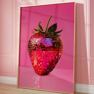 Op de afbeelding: Een ingelijste print met een aardbei-ontwerp. De aardbei is gemaakt van kleine, reflecterende, rode en roze vierkantjes, die lijken op een discobal. De achtergrond is effen roze en de lijst is goudkleurig.