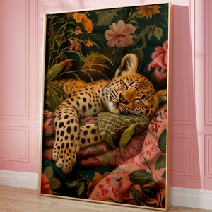 Puede incluir: Un cachorro de leopardo durmiendo con manchas marrones y negras, acostado sobre una almohada y una manta con estampado floral de colores. El fondo es verde oscuro con patrones florales en tonos de rosa, rojo y amarillo.