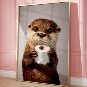 May include: A framed wall art print featuring a detailed illustration of a brown otter with large dark eyes holding a white roll of toilet paper. The otter has textured fur, long whiskers, and is centered within a thin gold-colored metal frame.