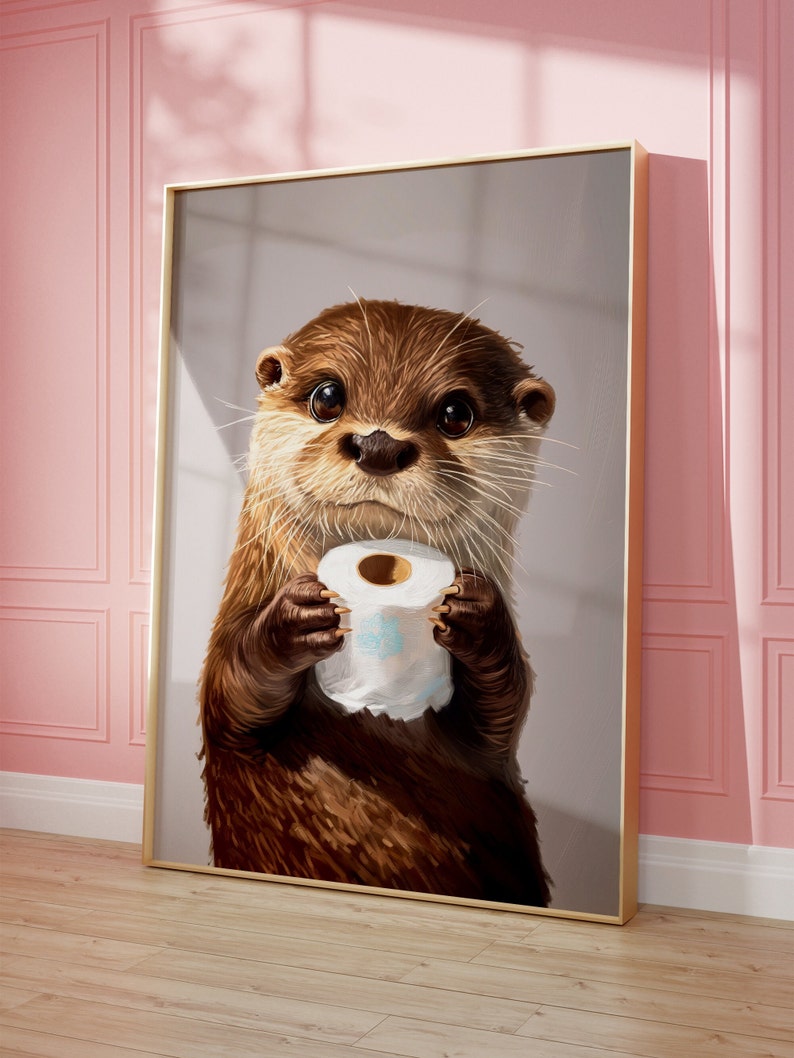 May include: A framed wall art print featuring a detailed illustration of a brown otter with large dark eyes holding a white roll of toilet paper. The otter has textured fur, long whiskers, and is centered within a thin gold-colored metal frame.