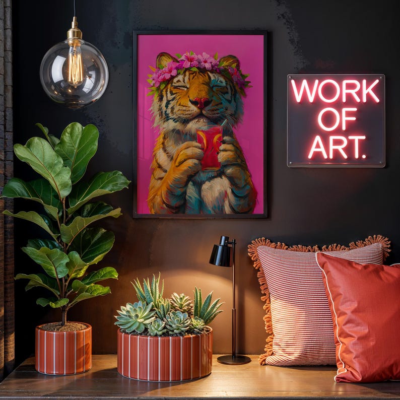 May include: A framed wall art print featuring a tiger wearing a pink flower crown and holding a red drink against a bright pink background. The print is displayed near a neon sign with the text WORK OF ART, a fiddle leaf fig, and succulents.