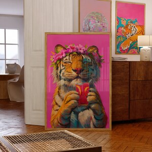 May include: A framed wall art print featuring a tiger with a pink flower crown, holding a glass of red liquid with a straw, set against a vibrant magenta background. The tiger has its eyes closed and is depicted in a painterly style with visible brushstrokes.