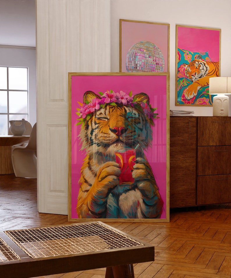 May include: A framed wall art print featuring a tiger with a pink flower crown, holding a glass of red liquid with a straw, set against a vibrant magenta background. The tiger has its eyes closed and is depicted in a painterly style with visible brushstrokes.