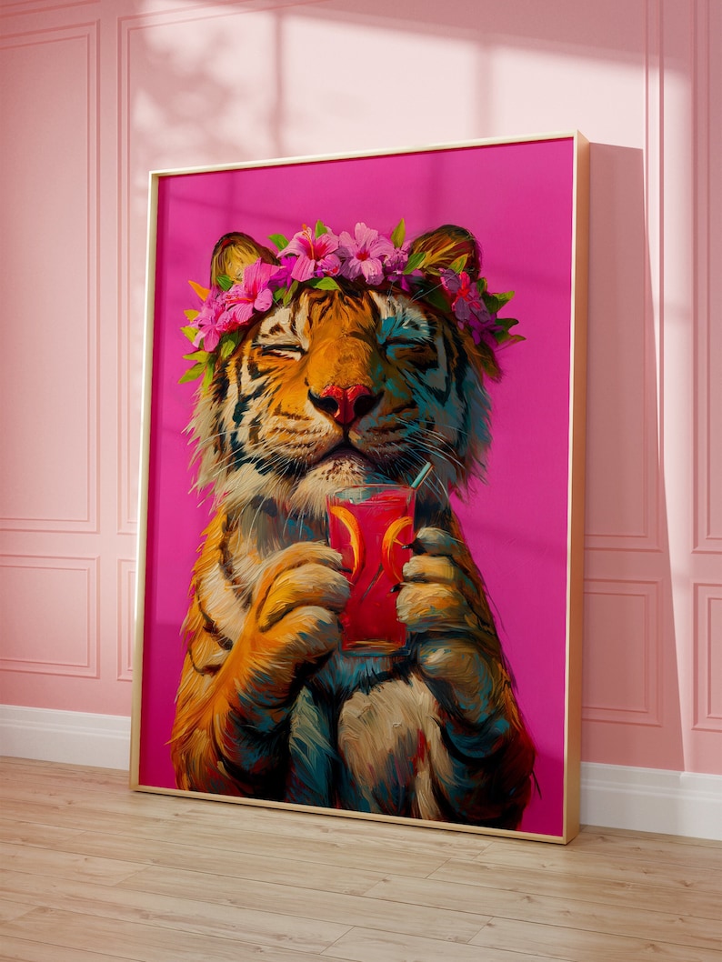May include: A framed wall art print featuring an orange and black tiger with closed eyes, wearing a crown of pink hibiscus flowers and green leaves. The tiger holds a glass of red liquid with orange slices and a straw against a bright pink background.