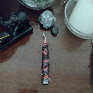 May include: A red and black candle with a white wick. The candle is decorated with a pattern of black and red.