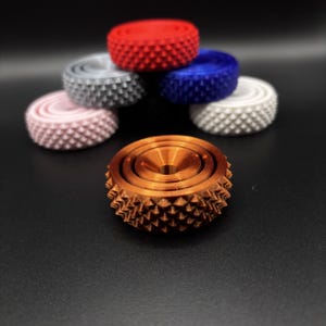 May include: A collection of colorful, textured, circular objects. The objects are in shades of red, blue, white, gray, pink, and bronze. The bronze object is in the foreground, with the other objects stacked in the background.